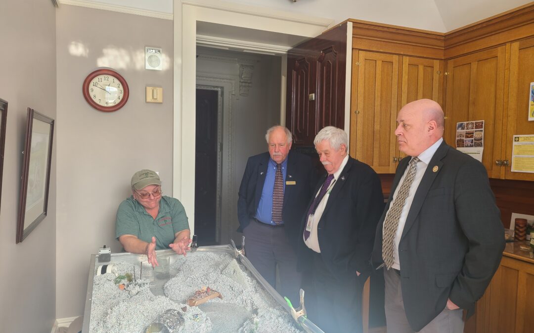 Kelly at the stream table with legislators looking on.